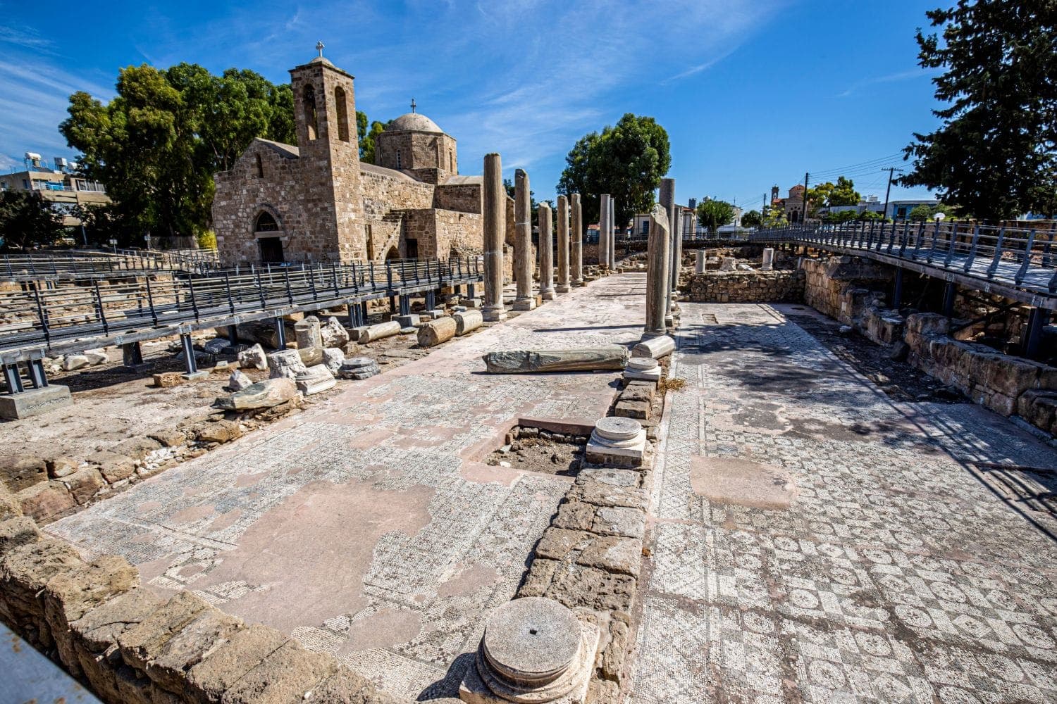 The stone church of Agia Kyriaki Chrysopolitissa behind the columns and mosaic floor of the early Christian basilica, seen from the visitor walkway