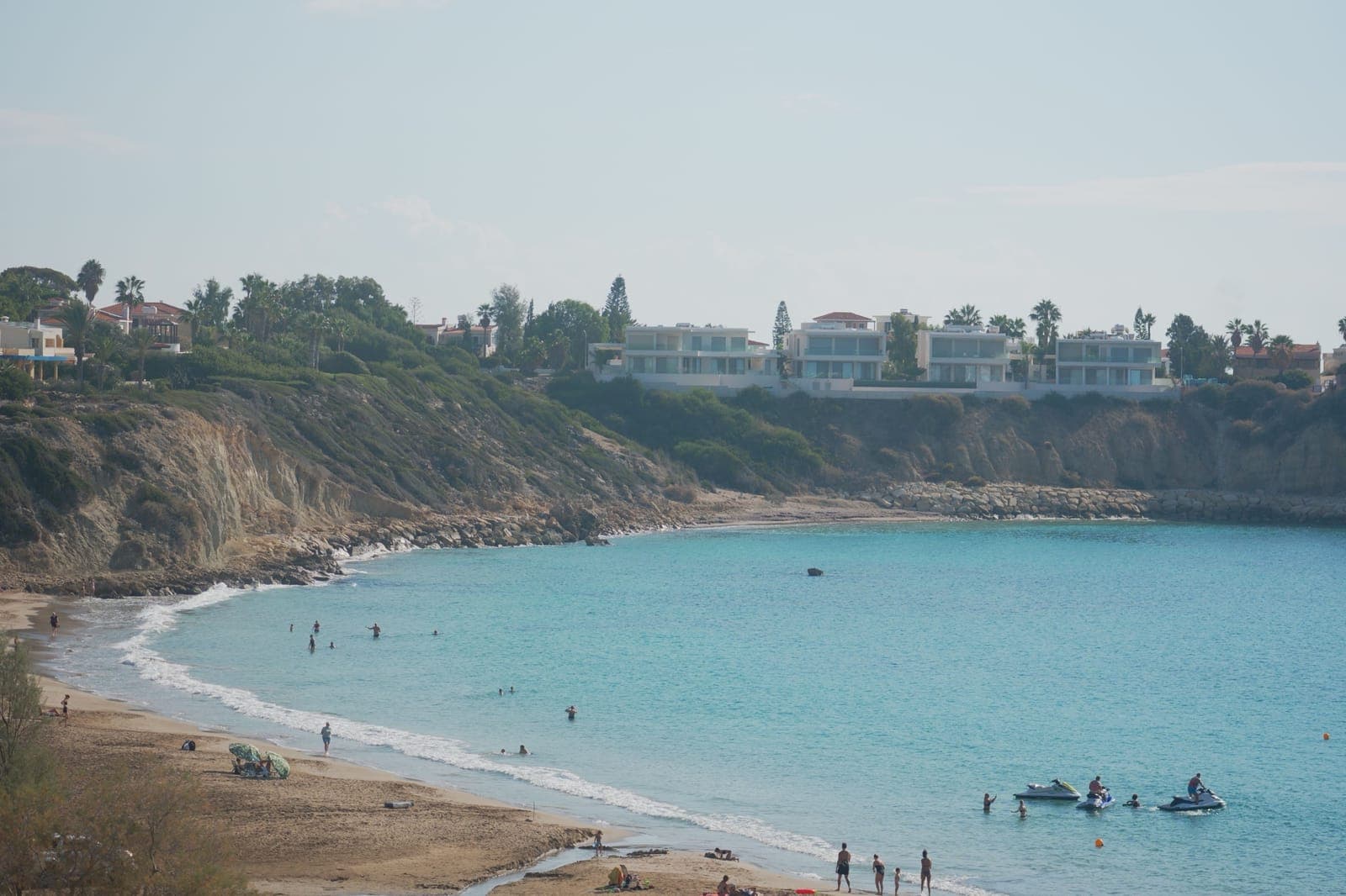 The sandy crescent of Coral Bay with swimmers in turquoise water, low cliffs and villas along the headland